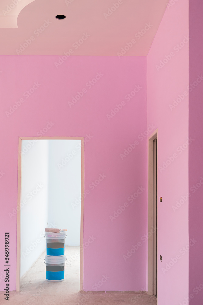 Paint roller with 2 plastic paint bucket in door frame with pastel pink cement wall inside of house construction site in vertical frame Paint roller with 2 plastic paint bucket in door frame with pastel pink cement wall inside of house construction site in vertical frame