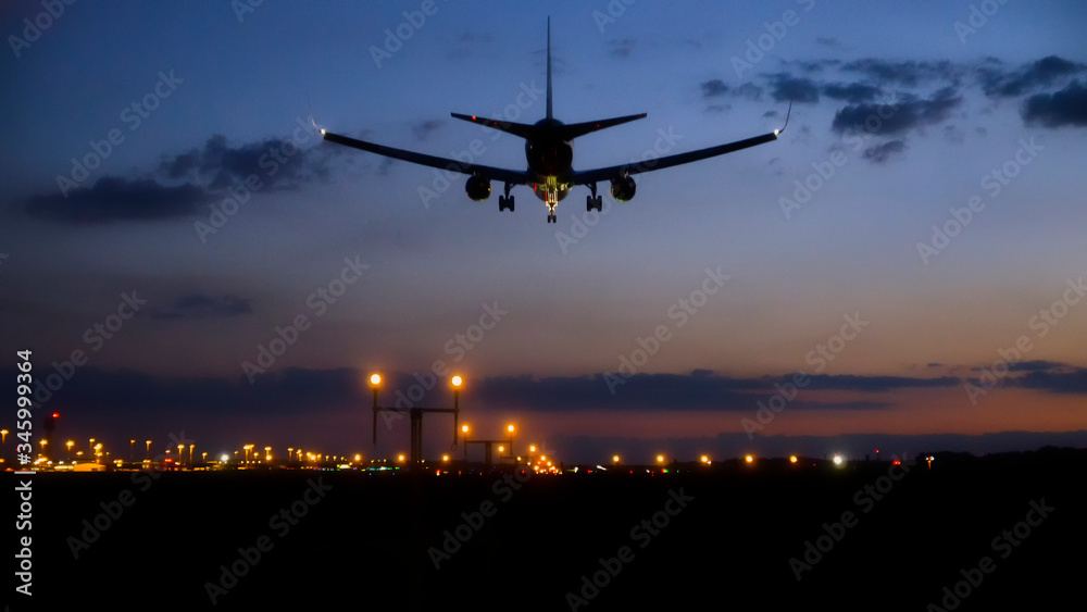 Commercial airliner landing above lighten up approach lights of international airport runway at sunset during blue hour with beautiful cloudy sky in the background