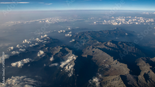 Beautiful aerial view on the Italian Alps on a sunny day with clear sky and low altitude clouds. Flying above mountains with some haze in background © Jetstream Rider