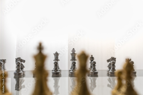 Sport board game, Business and planning concept. Closeup of King, Queen, Bishop, knight and pawn silver chess pieces face to face with gold pieces on glass table.