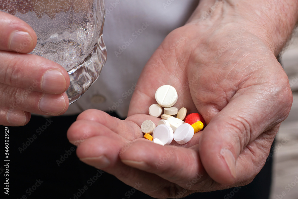 The hands of an elderly man hold a handful of colorful tablets and a glass of water. The concept of old age, diseases, medications, treatment. The hands of an elderly man hold a handful of colorful tablets and a glass of water. The concept of old age, diseases, medications, treatment.