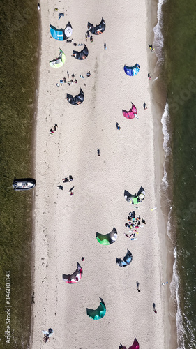 Aerial view of white sand beach peninsula with kites for kite surfing laying down on the beach and some kite surfers flying on the waves. Polish seaside coast with the Baltic Sea's waters.