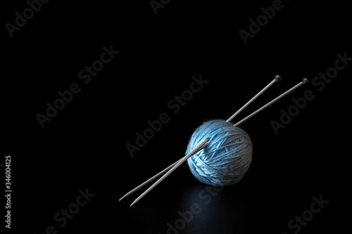 Blue ball of yarn with metal knitting needles on a black background