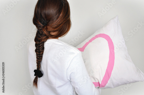 Chica de espaldas con una trenza abrazando la almohada. Fondo blanco. photo