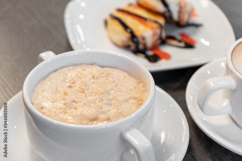 Oatmeal porridge on a wooden table near cheesecakes and cappuccino. Oatmeal porridge on a wooden table near cheesecakes and cappuccino.