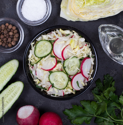 Vitamin salad of fresh vegetables cabbage, radishes, cucumbers and parsley in a bowl on a dark background top view