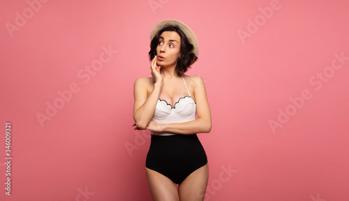 Fototapeta Naklejka Na Ścianę i Meble -  Portrait of a gorgeous trendy fit woman in swimwear while she enjoying rest with sunlight isolated over pink background. Travel, tourism, journey, trip, tour, summer concept