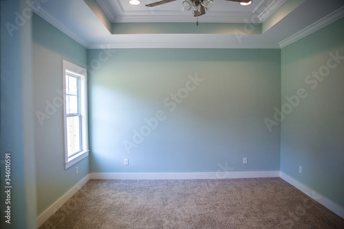 White tray master bedroom ceiling in small new construction house with windows and a ceiling fan and pale blue turquoise walls