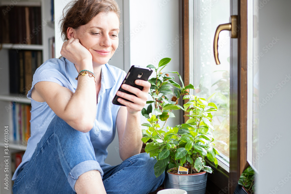 happy woman using smartphone at home by window social media connection happy woman using smartphone at home by window social media connection
