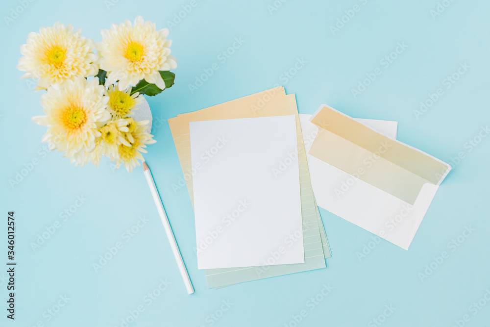 Mockup white wedding invitation and envelope with flowers in a vase on a blue background Mockup white wedding invitation and envelope with flowers in a vase on a blue background