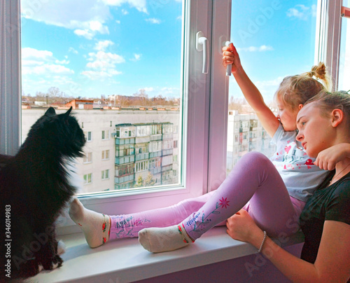 girl together with cat looking sadly out window staying home during quarantine photo