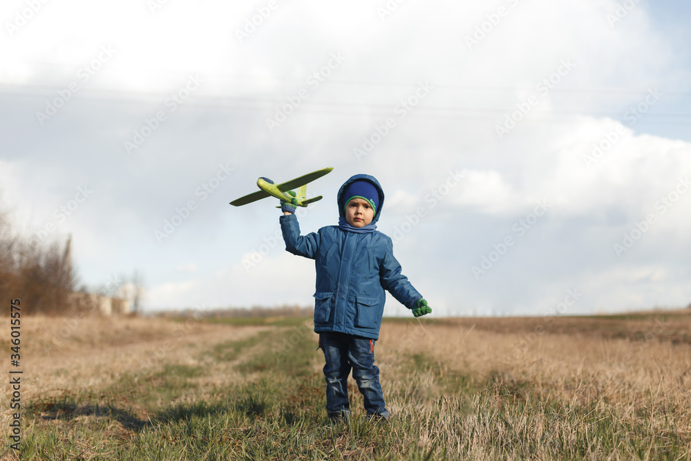 The boy is standing in the dry grass, looking into the camera, dreaming and holding a green airplane. The boy is standing in the dry grass, looking into the camera, dreaming and holding a green airplane.