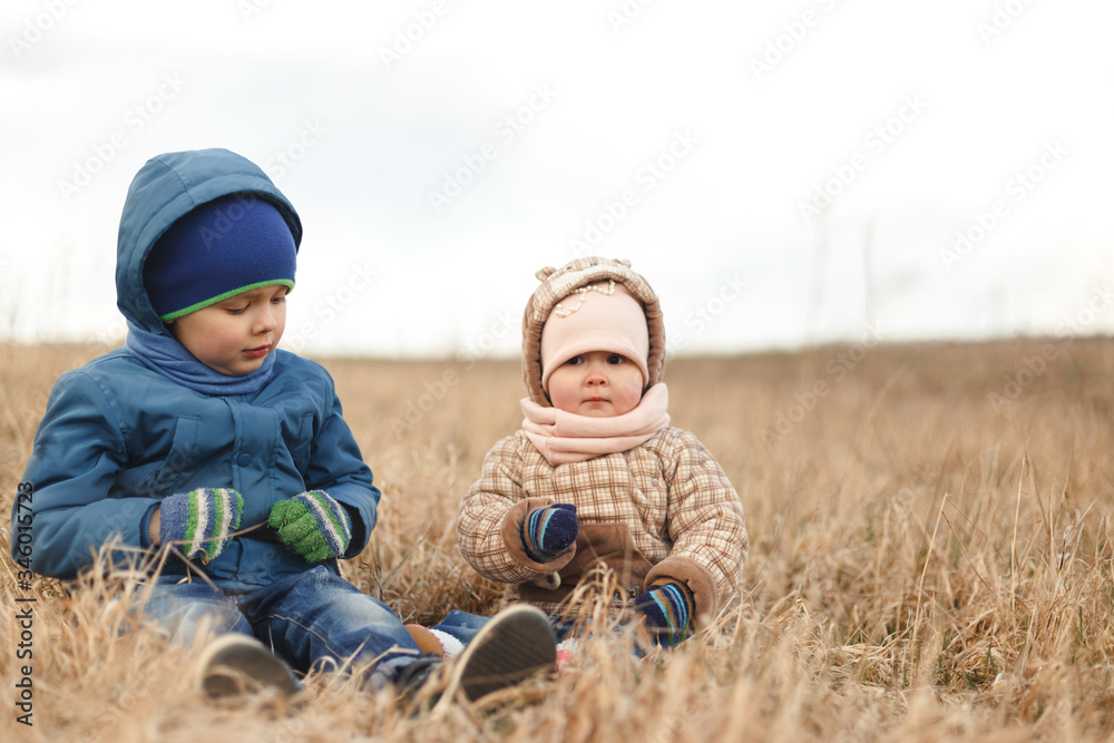 Brother and sister sitting in the dry grass in the spring in the field. Brother and sister sitting in the dry grass in the spring in the field.