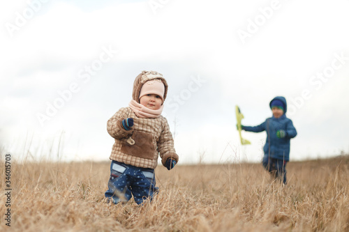 Little baby girl standing in the field of dry grass and her brother with toy airplane. Portrait  with background of white sky.
