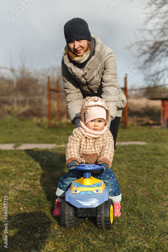 Mother help her daughter to ride on the toy car.