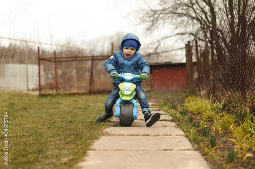 Little boy riding on the toy motobike in the yard.