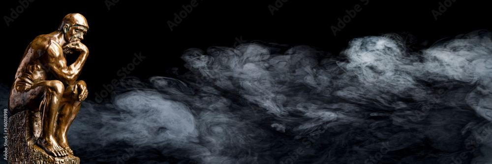 A bronze replica statue of Rodin's Thinker on a smoky background A bronze replica statue of Rodin's Thinker on a smoky background