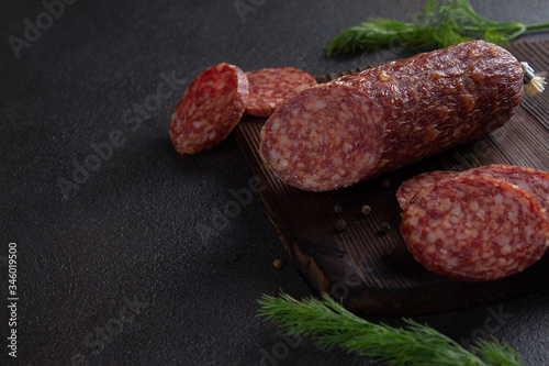 Dark banner of smoked sausage. Sausage cut from meat on a wooden Board with herbs and black pepper. Gloomy mood. Creative and delicious serving. Low key. Copy space