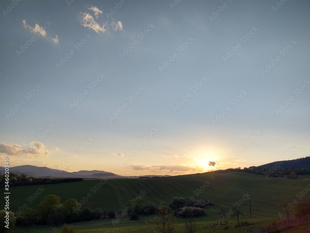 Fototapeta premium Sunrise and sunset, beautiful clouds over the meadow, hills and buildings in the town. Slovakia