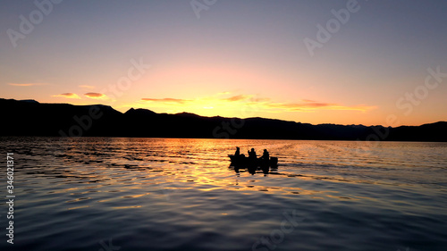 4 people fishing in a boat floating on Hebgen Lake during colorful sunset.