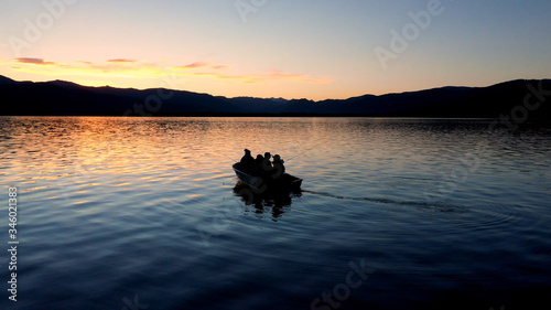 Person pull starting motor of boat floating on Hebgen Lake during colorful sunset.