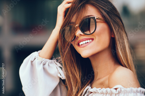 Portrait of a beautiful young woman with smile and sunglasses in the city photo