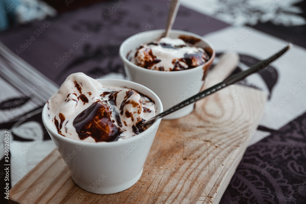 Containers with vanilla ice cream and liquid chocolate ready to eat on a wooden board Containers with vanilla ice cream and liquid chocolate ready to eat on a wooden board