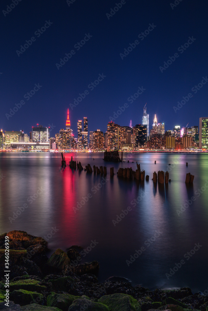 Obraz premium Midtown Manhattan at night from East river ,Empire state building is in red lights