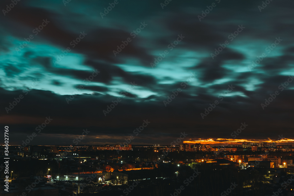 Twilight landscape of dark blue sky with black clouds and city lights. Scenic sunset. Panorama of night town. Dramatic and gloomy cityscape. Long exposure with cloud movement