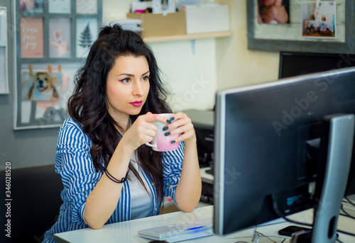 beautiful creative girl sitting at a desk in front of a computer monitor. Designer reflects and thinks on a project