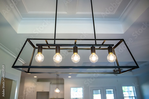 Hanging retro black metal iron chandelier lighting fixture with vintage bulbs hanging in a dining room of a new construction house photo
