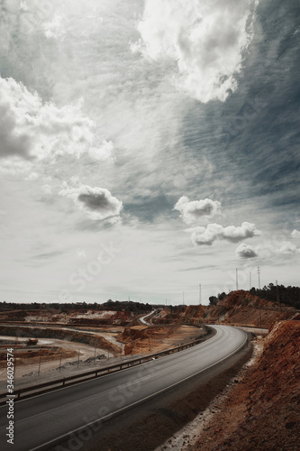 Empty asphalt road outside the city in a curve with a dramatic cloudy day in Huelva, Spain. The road is next to a quarry of red sand