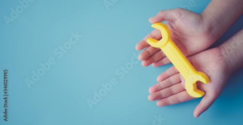 Kid girl hands holding yellow wrench toy on blue background.Concept for brain fix, child development, Broken family, Renovate home, Recovery mind, Engineer education, Learn creative kid, Workshop.