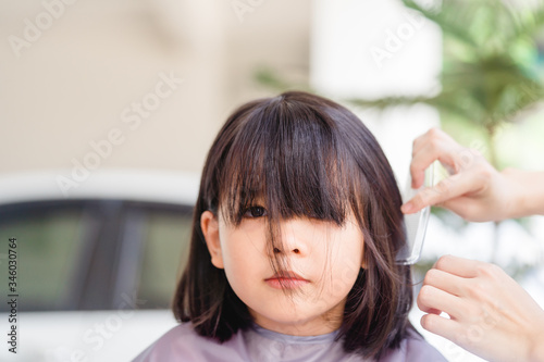 Asian Mother cutting hair to her daughter by herself at home.Stay at home stay safe from Covid-19 Coronavirus.Hairstyle online class, Stay home and life during lockdown.Happy smiley face from kid girl © MIA Studio