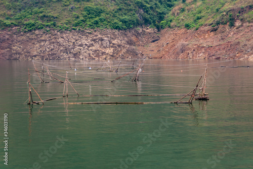 Wuchan, China - May 7, 2010: Dicui Gorge on Daning River. Closeup of fish pens in emerald green water in front of brown stone shoreline with green foliage on top. photo