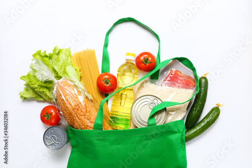 Set of grocery items from vegetables, canned food, pasta, oil, cereal in green eco shopping bag on white background. Top view.