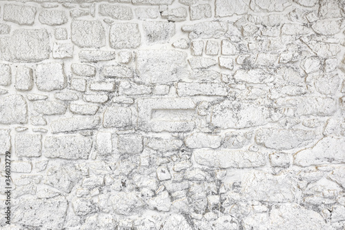 Old rustic natural stone wall background, whitewashed with peeling paint