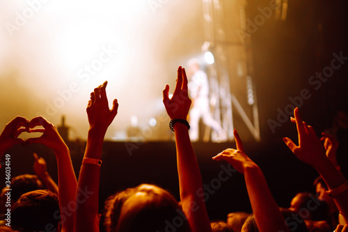 Сrowd with raised hands at music festival. Fans enjoying rock concert with light show and clapping hands.