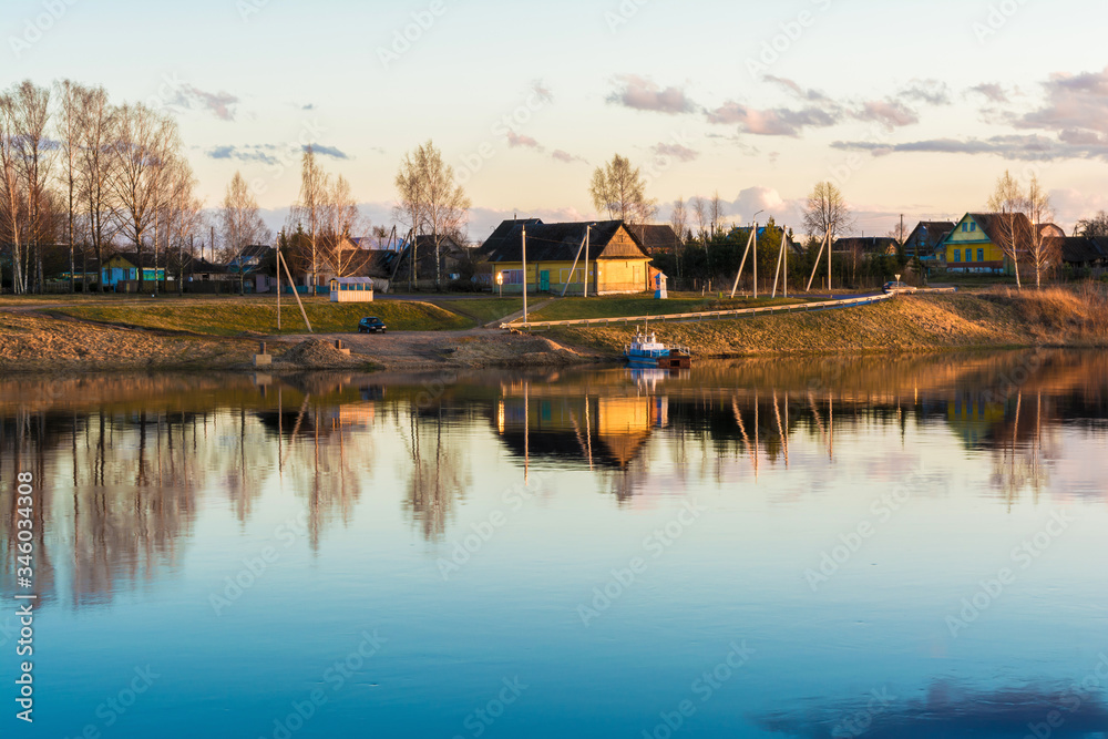 Obraz premium urban village or village with wooden houses located on the blue river bank, early spring evening at sunset