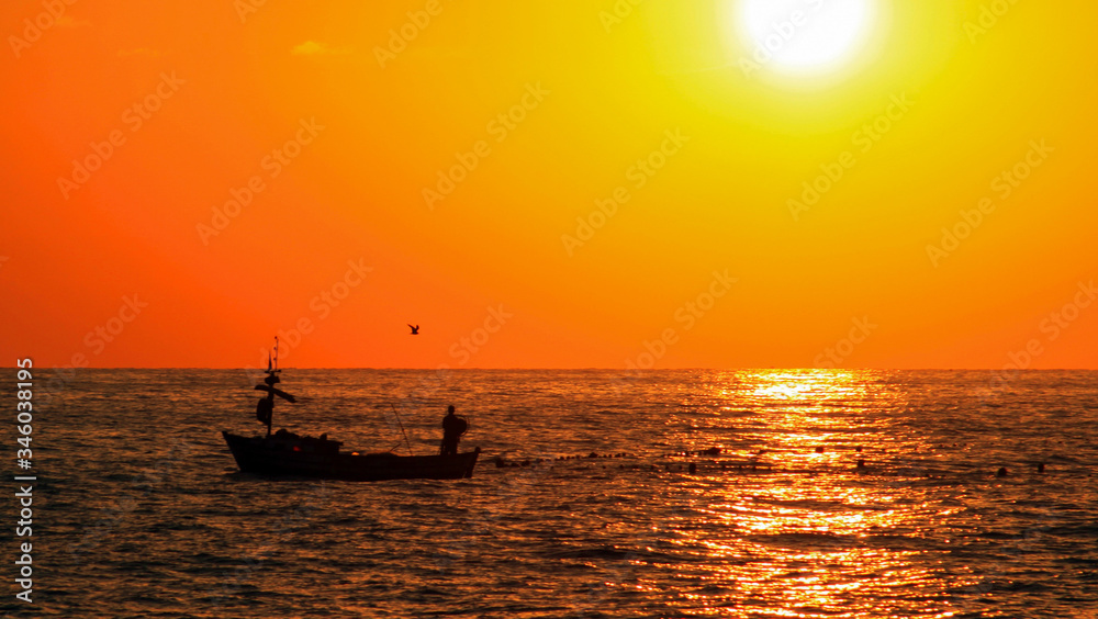 Fisherman in boat on the sea before sunset