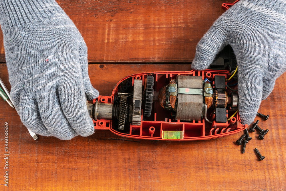 Technician repairs old electric drill on brown wooden table Technician repairs old electric drill on brown wooden table