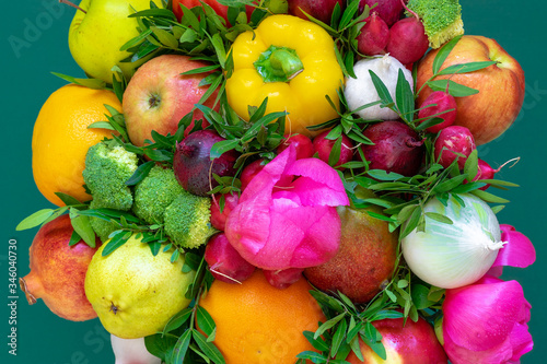 Wonderful  unconventional  multicolored floristic arrangement with fruits  vegetables  peonies and leaves on a green background. Close up  top view