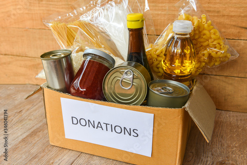 Donations box with canned food on wooden table background / pasta canned goods and dry food non perishable with cooking oil rice noodles spaghetti macaroni donations food