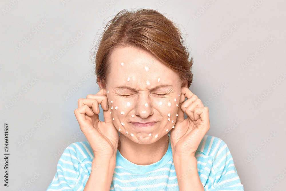 Portrait of annoyed girl with white drops of face cream on skin Portrait of annoyed girl with white drops of face cream on skin