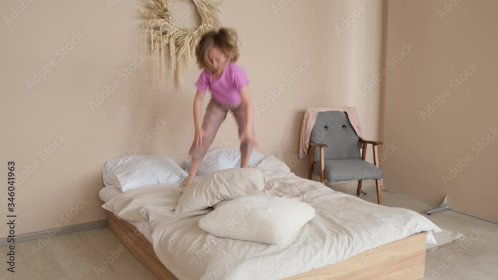 The girl dances on the bed, falls on the pillows and tumbles. Side view The girl dances on the bed, falls on the pillows and tumbles. Side view