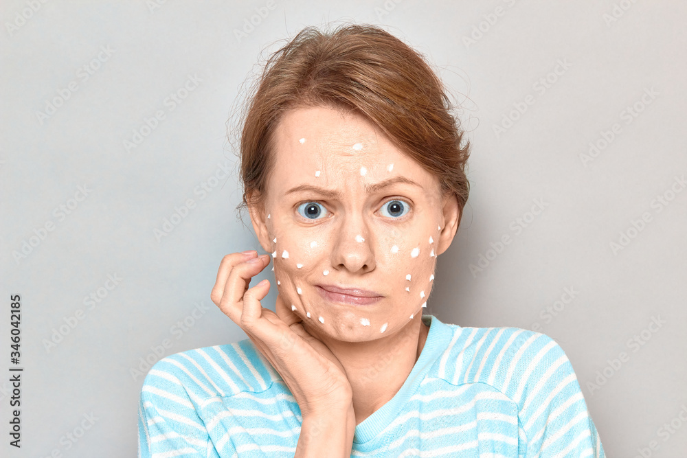 Portrait of unhappy sad girl with white drops of face cream on skin