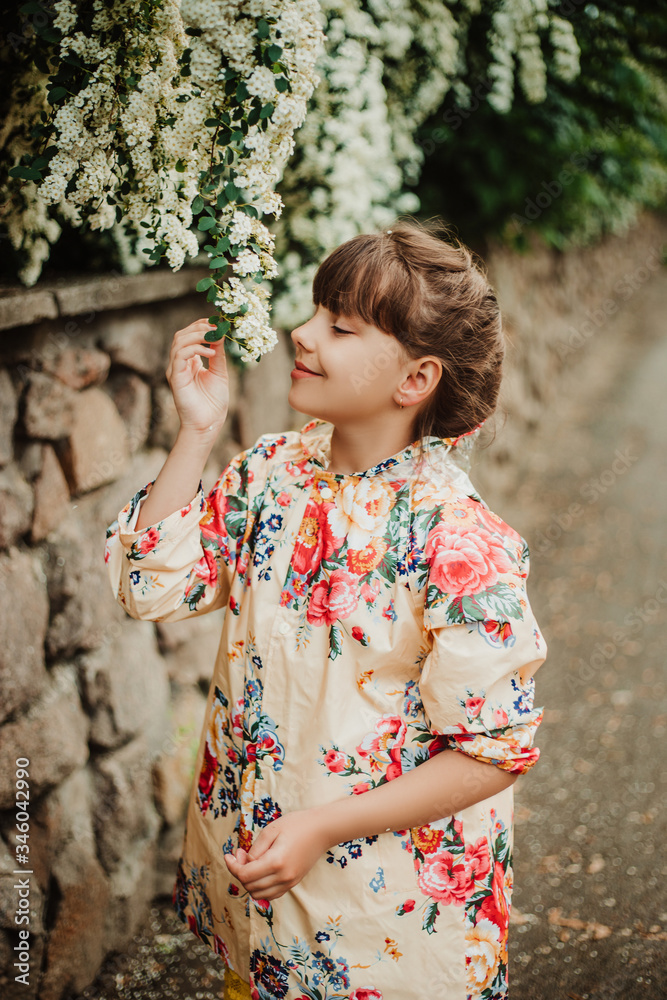 Beautiful girl in a bright raincoat walks after the rain in the park. Excellent spirea flowering bushes. Soft focus. Happy childhood concept