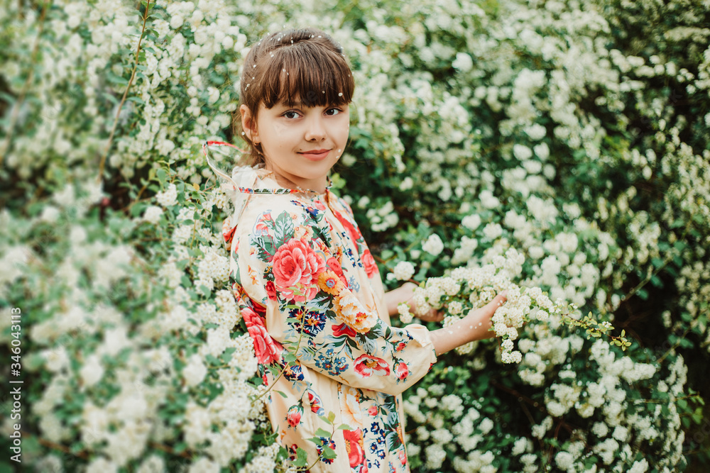 Beautiful girl in a bright raincoat walks after the rain in the park. Excellent spirea flowering bushes. Soft focus. Happy childhood concept Beautiful girl in a bright raincoat walks after the rain in the park. Excellent spirea flowering bushes. Soft focus. Happy childhood concept