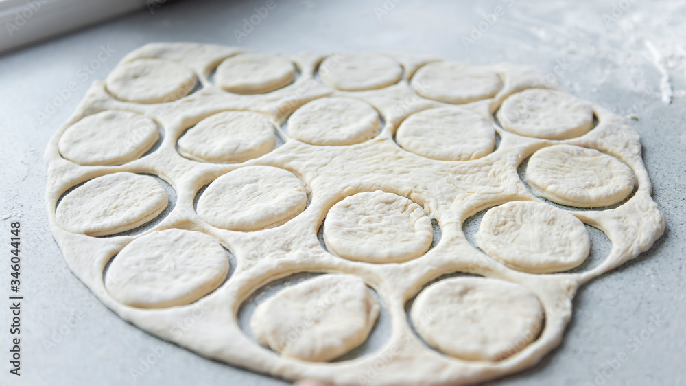 Preparation of the dough for baking, freezing, sculpting and other food blanks - a large piece of the dough is on the table and the chef cuts out small circles on it with an iron shape. Moulding Preparation of the dough for baking, freezing, sculpting and other food blanks - a large piece of the dough is on the table and the chef cuts out small circles on it with an iron shape. Moulding