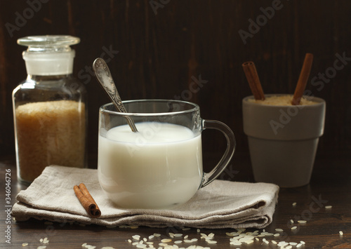 Vegetable milk in a glass Cup on a dark wooden background with cinnamon and rice grains